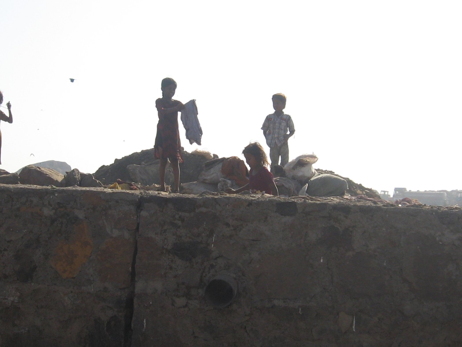 Children standing on a mound of waste against the sky