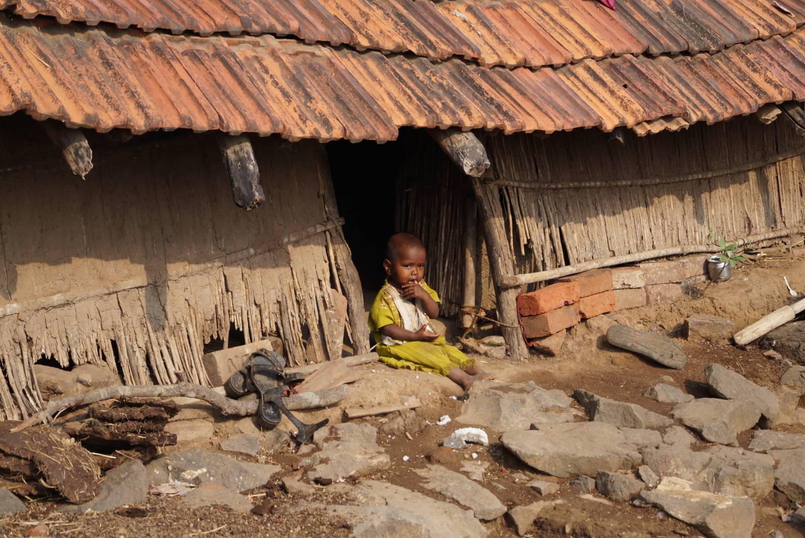 A child sitting at the door of a thatched hut